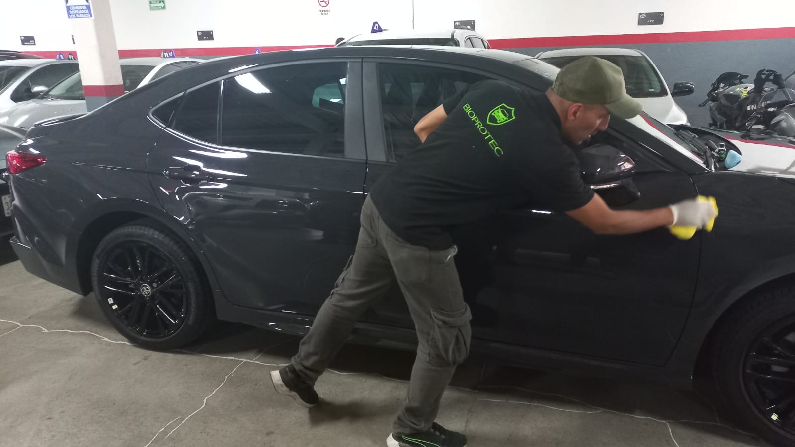 Técnico BioProtec aplicando protección en un sedán gris en estacionamiento